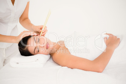 Beautiful woman receiving ear candle treatment at spa center