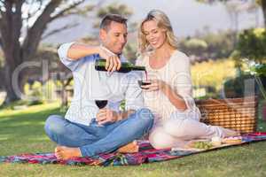 Smiling couple sitting on picnic blanket and pouring wine in gla