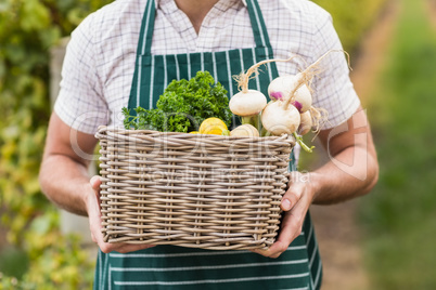 Young happy farmer holding a basket of vegetables