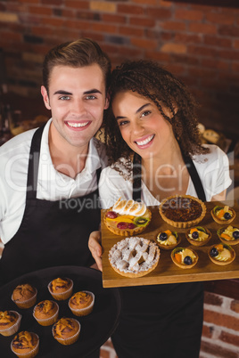 Smiling waiter and waitress holding tray with muffins