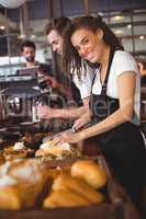 Smiling waitress cutting bread in front of colleague