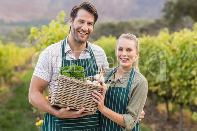 Two young happy farmers holding a basket of vegetables