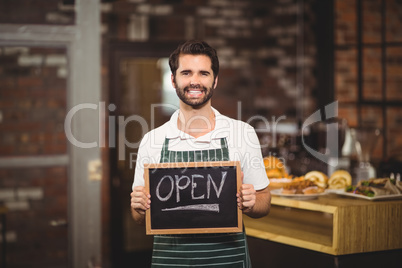 Smiling waiter showing chalkboard with open sign