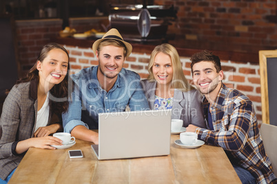 Smiling friends drinking coffee and using laptop