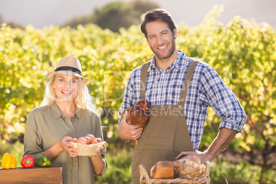 Smiling farmer couple holding chicken and eggs