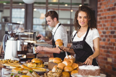 Smiling waitress holding bread roll with tong