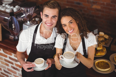 Smiling waiter and waitress holding cup of coffee