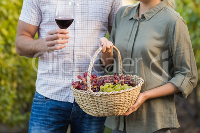 Two young happy vintners holding a basket of grapes and a glass