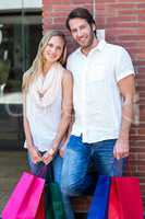 Smiling couple with shopping bags leaning on the wall