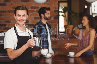 Smiling barista pouring milk into cup in front of customers