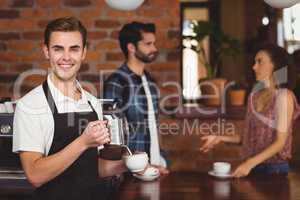 Smiling barista pouring milk into cup in front of customers