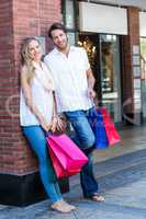 Smiling couple with shopping bags leaning on the wall