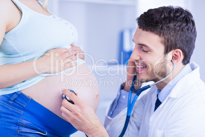 Smiling doctor examining stomach of standing pregnant patient