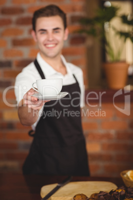 Smiling barista offering cup of coffee to camera