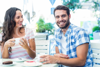 Cute couple sitting outside at a cafe with man smiling at camera