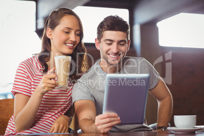 Smiling friends drinking coffee and looking at tablet computer