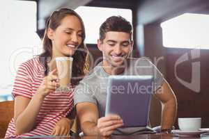 Smiling friends drinking coffee and looking at tablet computer