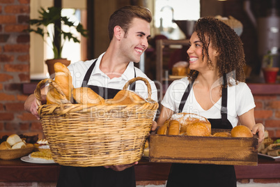 Smiling waiter and waitress holding basket full of bread rolls
