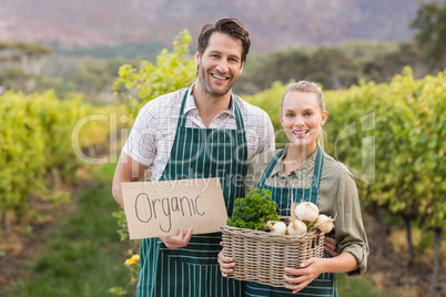 Two young happy farmers holding a sign and a basket of vegetable