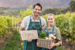 Two young happy farmers holding a sign and a basket of vegetable