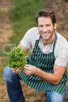 Young happy farmer looking at camera while holding vegetable