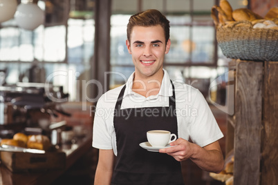 Smiling barista offering cup of coffee to camera