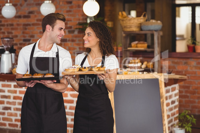 Smiling waiter and waitress holding tray with muffins