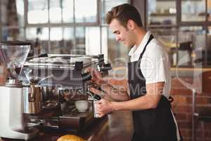 Smiling barista steaming milk at coffee machine