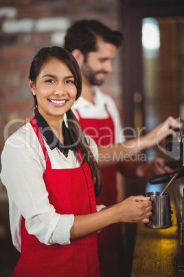 Smiling waitress steaming milk at the coffee machine