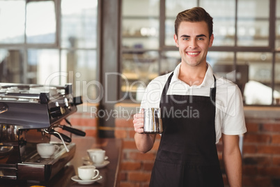 Smiling barista holding jug with milk