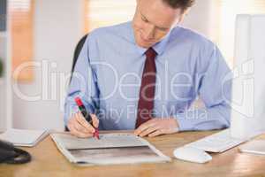 Businessman marking the newspaper with marker