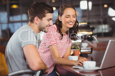 Smiling friends using laptop and having coffee together