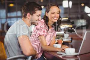 Smiling friends using laptop and having coffee together