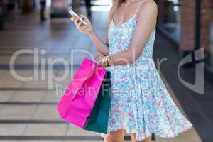 Woman walking with shopping bags and holding smartphone