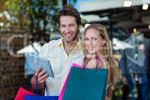 Smiling couple with shopping bags holding tablet computer