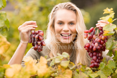 Smiling blonde winegrower holding red grapes