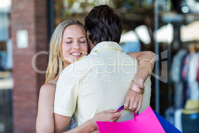 Smiling woman with shopping bags hugging her boyfriend