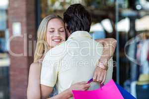 Smiling woman with shopping bags hugging her boyfriend
