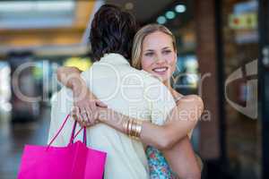 Smiling woman with shopping bags hugging her boyfriend