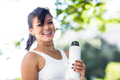 Portrait of smiling athletic woman holding water bottle and look