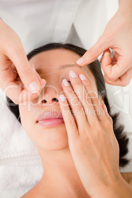 Hands threading beautiful womans eyebrow