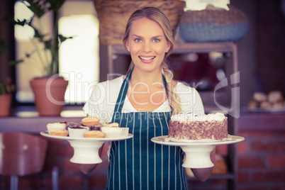 Pretty waitress holding a chocolate cake and cupcakes
