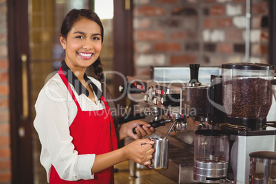 Smiling barista steaming milk at the coffee machine