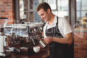 Smiling barista pouring milk into cup
