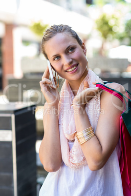 Smiling woman with shopping bags calling with mobile phone