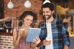 Smiling hipster couple with take-away cups using tablet