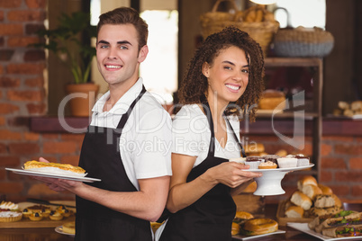 Smiling waiter and waitress holding plates with treat