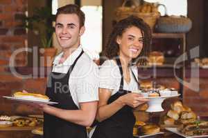 Smiling waiter and waitress holding plates with treat