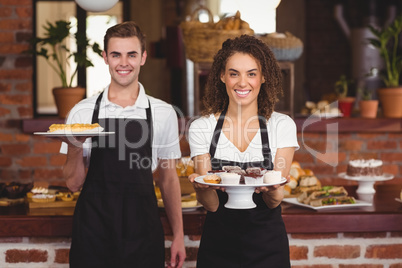 Smiling waiter and waitress showing plates with treat
