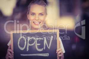 Smiling blonde waitress showing chalkboard with open sign